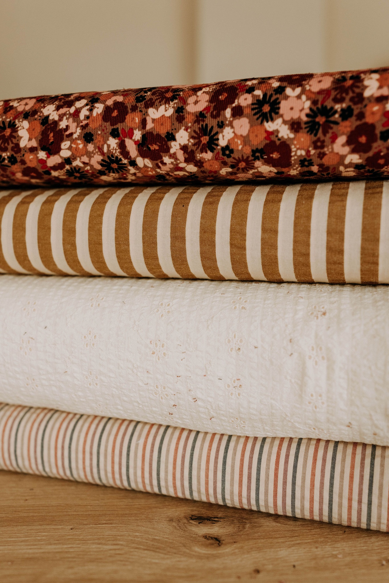 Quatre rouleaux de tissus empilés : motif fleuri, rayures, broderie anglaise et fines rayures