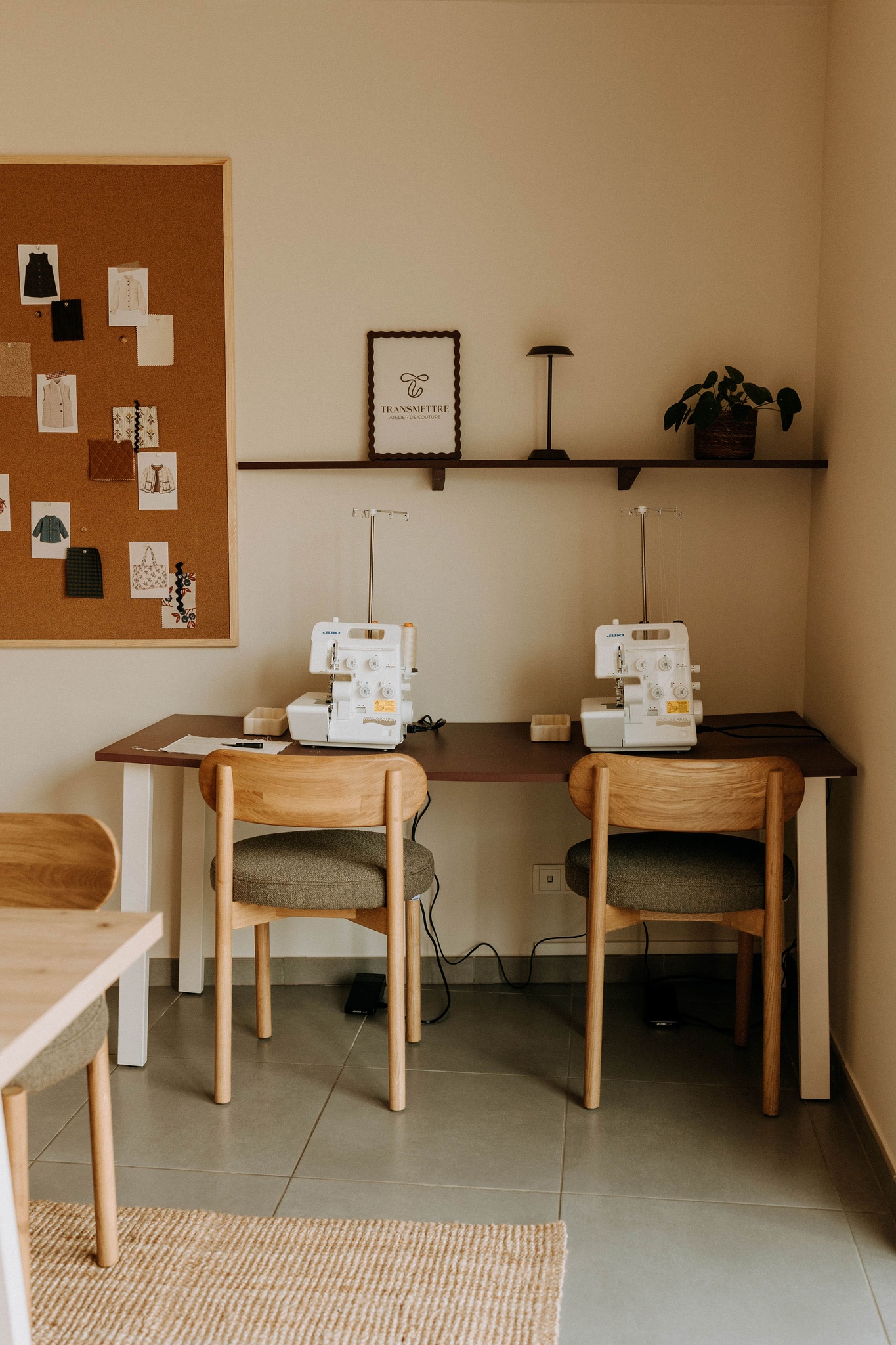 Postes de couture de l'atelier : deux machines posées sur une grande table, devant un mur de croquis