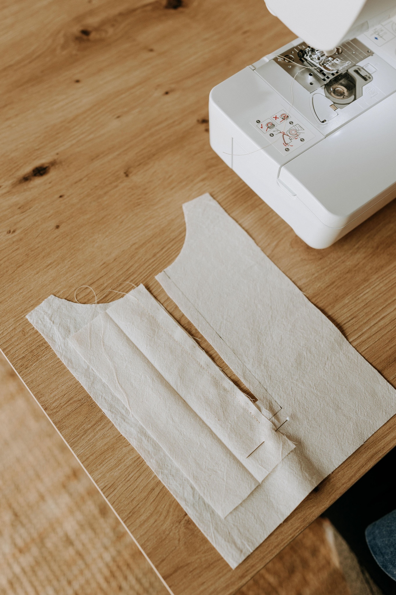 Une machine à coudre blanche et deux pièces de tissu clair posées sur la table de l'atelier