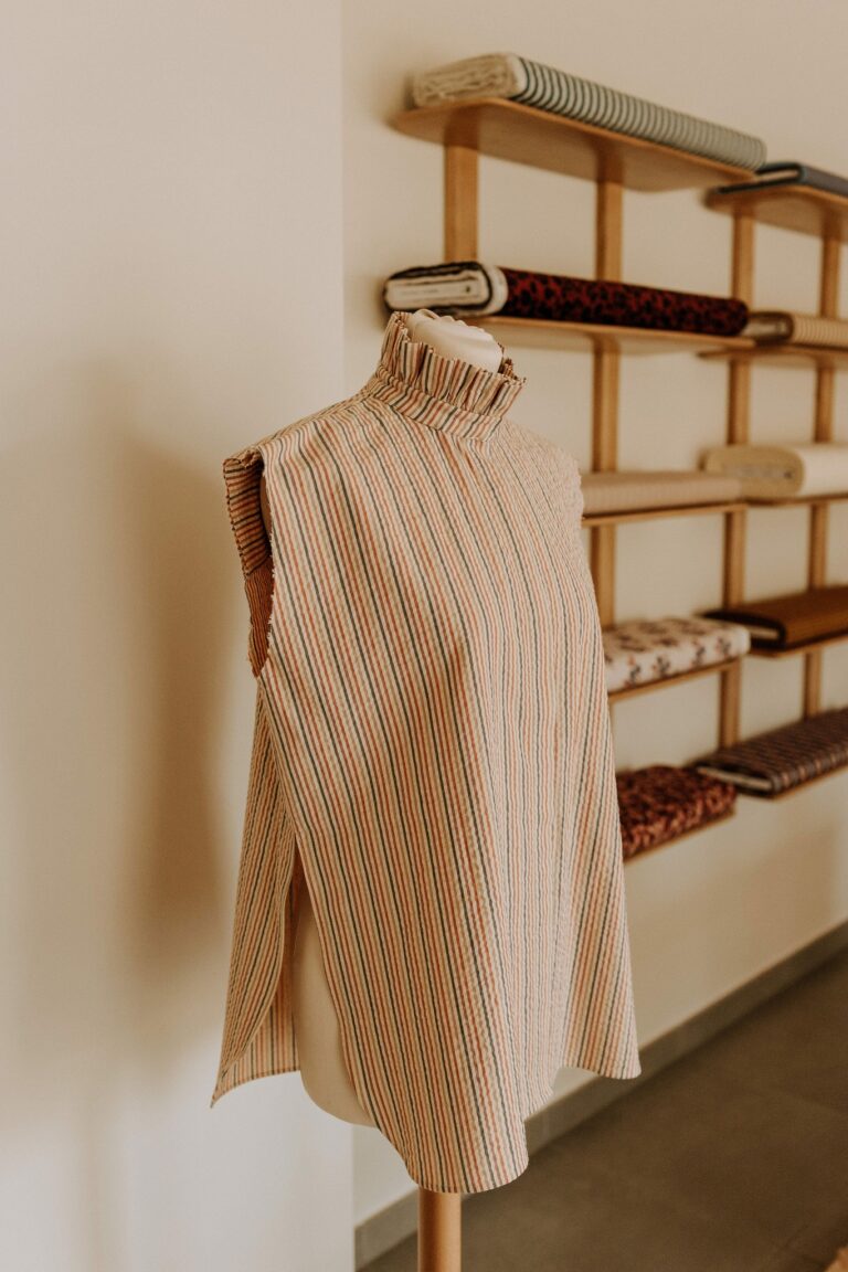 Blouse sans manches à col haut et fines rayures, présentée sur un mannequin de couture dans l'atelier