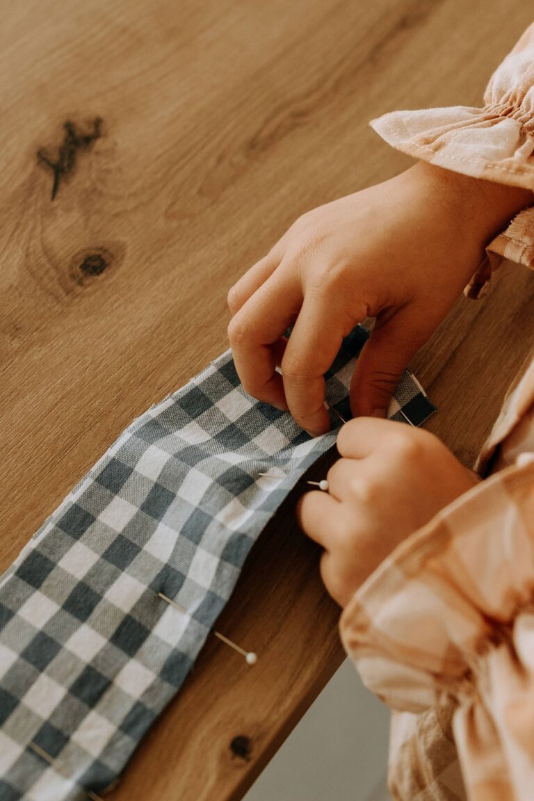 Mains épinglant une bande de tissu à carreaux bleus sur la table de coupe
