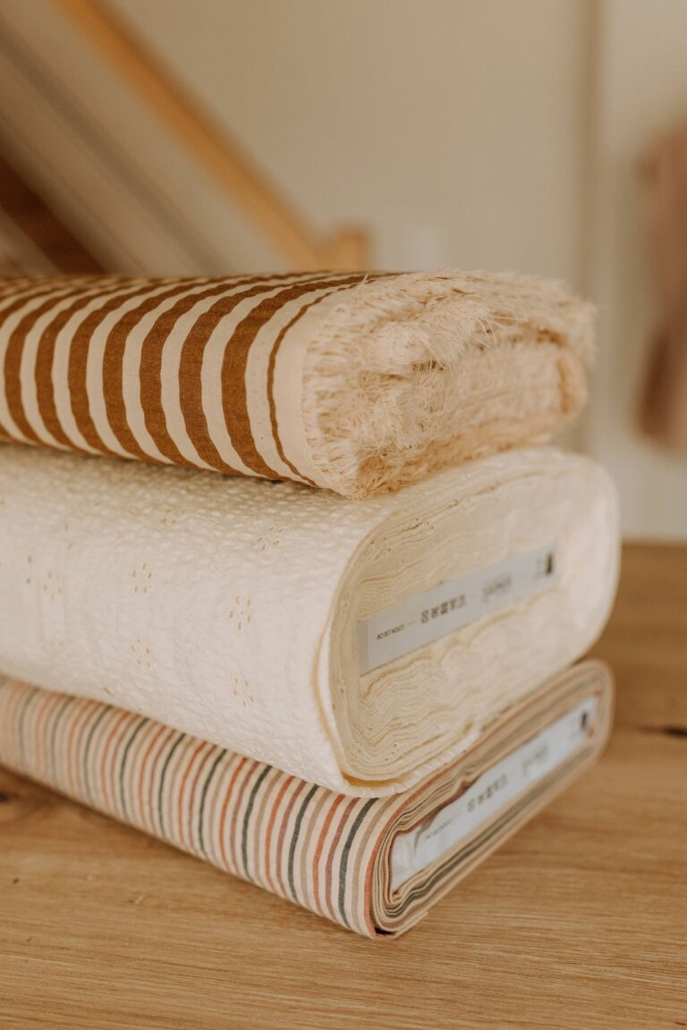 Trois rouleaux de tissu posés sur le bois de l'atelier : rayures larges, motif floral et fines rayures multicolores
